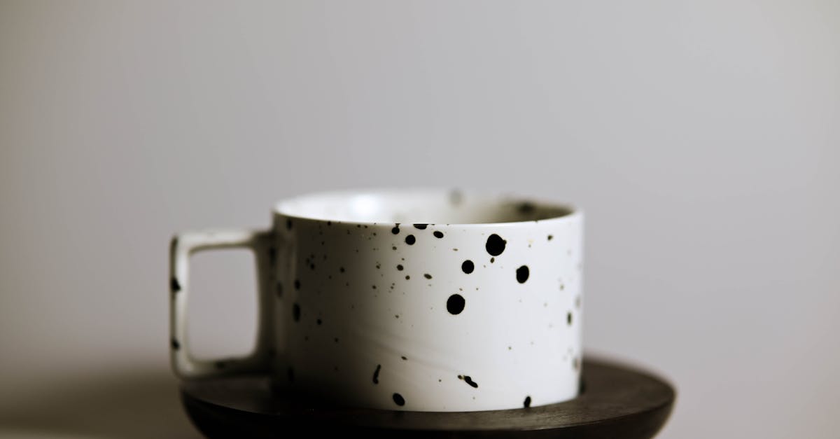 A minimalist black and white speckled coffee cup on a wooden saucer, perfect for a stylish coffee setting.
